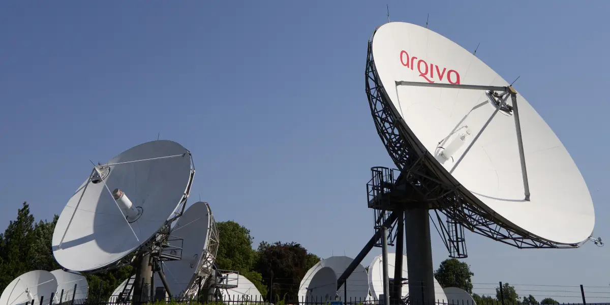 Ground station satellite dishes pointing to the sky. One dish has the words Arqiva visible on it in red lettering